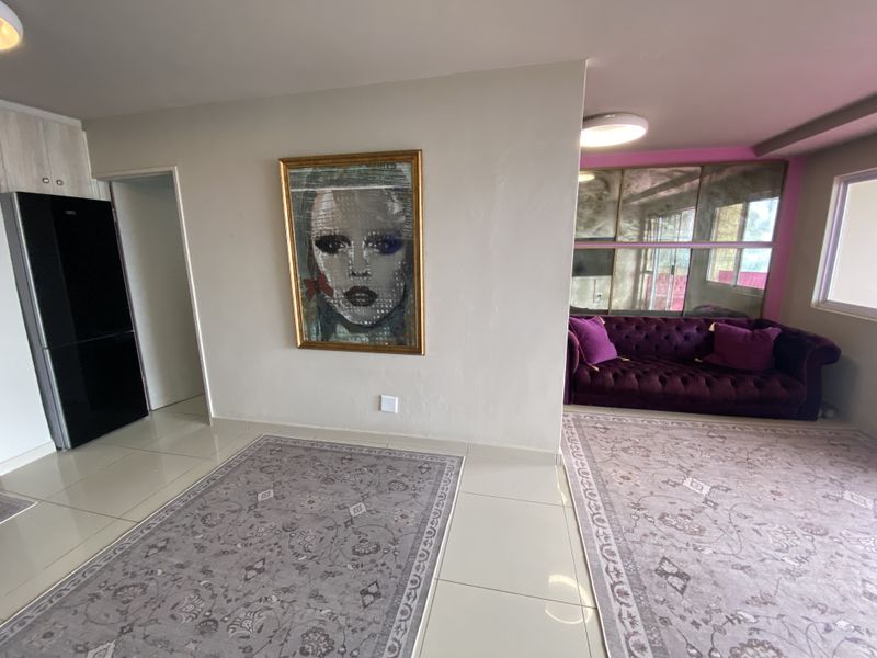 Open plan living area featuring large format floor tiles, mirrored wall accents, and integrated ceiling lighting, creating a bright and versatile living space.