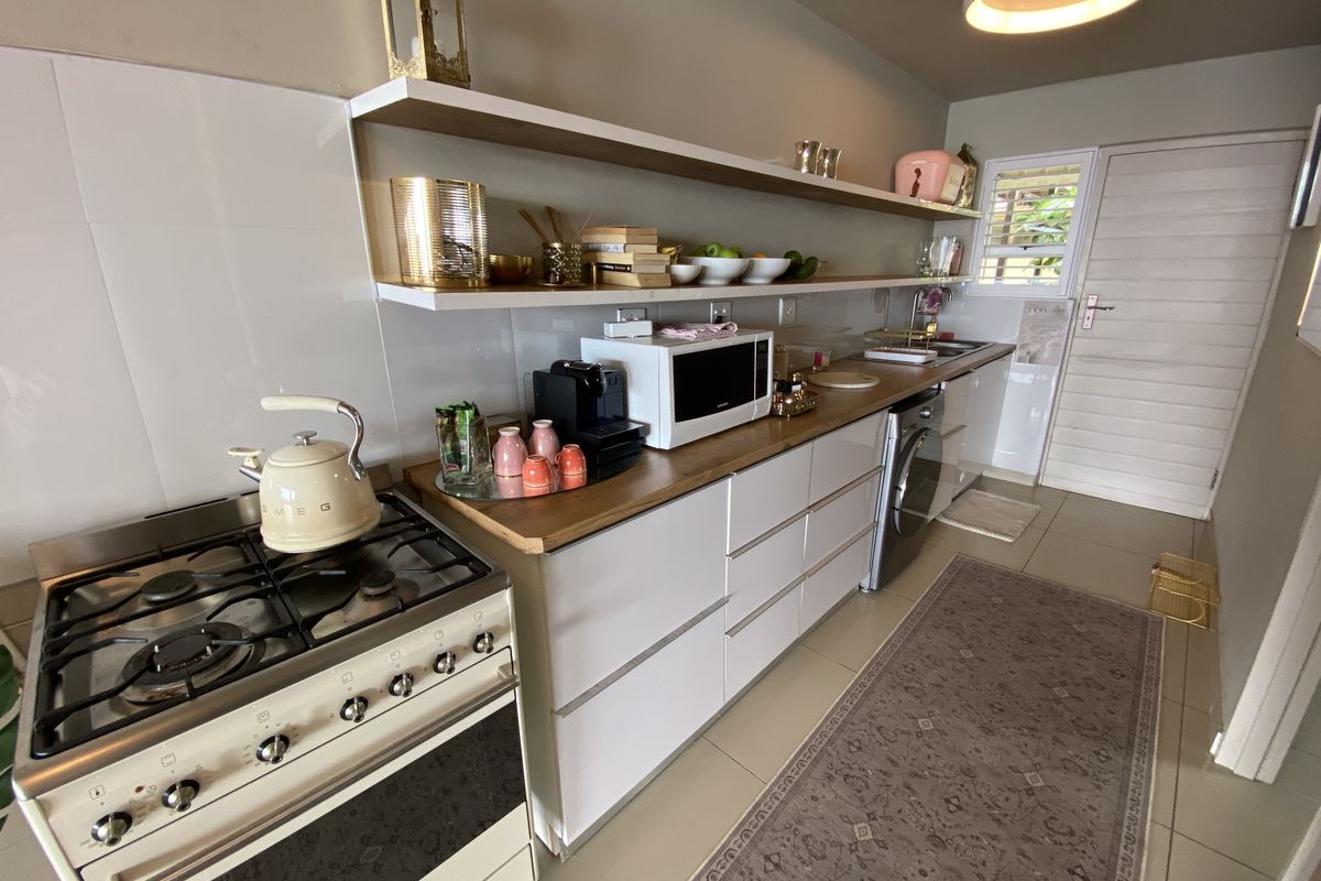 A modern, well-maintained kitchen featuring a gas stove, wooden countertops, floating shelving, and integrated laundry appliances.
