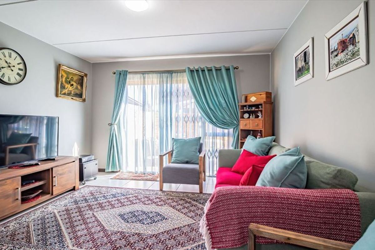 A well-maintained living room featuring tiled flooring and a sliding glass door with security gate, providing direct access to the outdoor area.