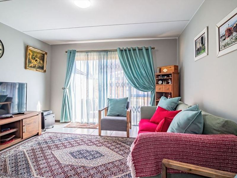 A well-maintained living room featuring tiled flooring and a sliding glass door with security gate, providing direct access to the outdoor area.