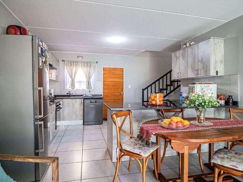 Open-plan kitchen and dining area featuring tiled flooring, granite countertops, built-in cabinetry, and a staircase leading to the upper level.