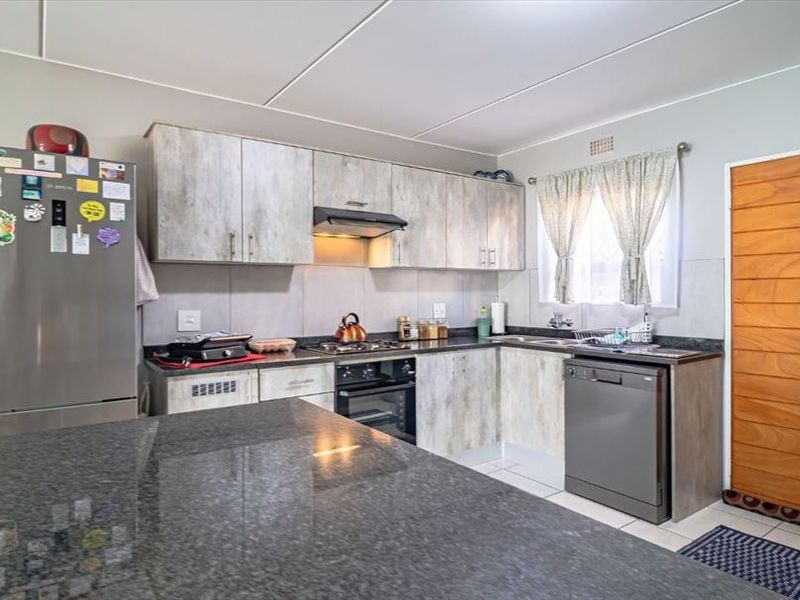 A functional kitchen featuring light wood-look cabinetry, granite countertops, built-in oven, hob, extractor fan, and tiled flooring.