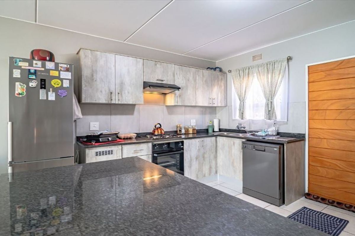 A functional kitchen featuring light wood-look cabinetry, granite countertops, built-in oven, hob, extractor fan, and tiled flooring.
