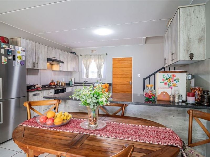 Open-plan kitchen and dining area featuring modern cabinetry, granite countertops, integrated hob, and tiled flooring, with an adjacent staircase.