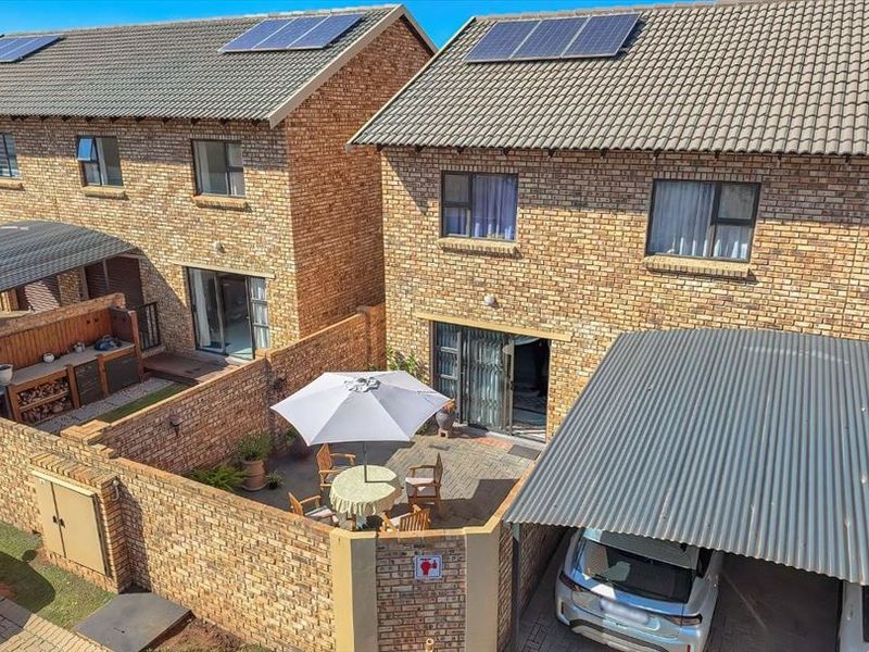 Aerial view of a facebrick cluster home featuring a private paved courtyard, carport, and roof-mounted solar panels.