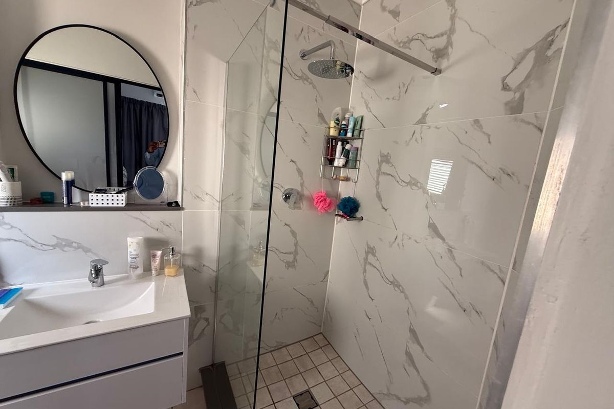 Modern bathroom featuring a sleek vanity with basin, round mirror, and a spacious walk-in shower with marble-look wall tiles and rainfall shower head.