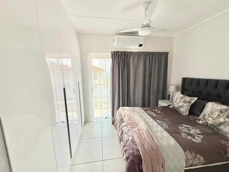 A well-maintained bedroom featuring built-in high-gloss cupboards, tiled flooring, a ceiling fan, and a split-system air conditioner with access to a balcony.