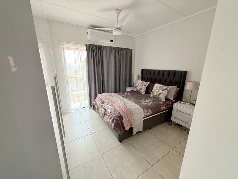 A well-maintained bedroom featuring tiled flooring, a ceiling fan, a split-system air conditioner, and direct access to a balcony through a sliding glass door.