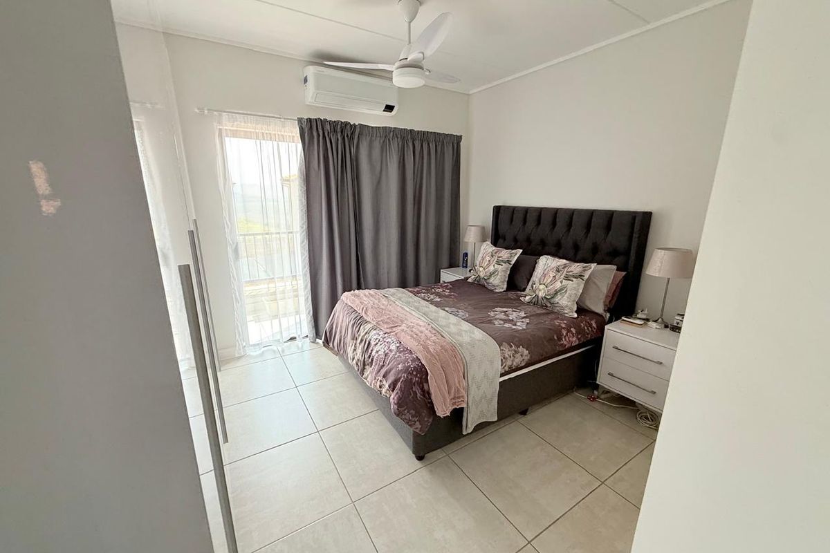A well-maintained bedroom featuring tiled flooring, a ceiling fan, a split-system air conditioner, and direct access to a balcony through a sliding glass door.
