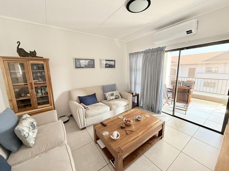 Bright living room featuring tiled flooring, a wall-mounted air conditioning unit, and large sliding glass doors providing access to an outdoor balcony area.