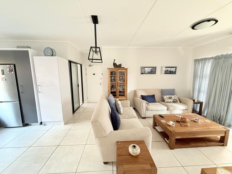 An open-plan living area featuring neutral tiled flooring, modern pendant lighting, and clean white walls, creating a bright and functional living space.