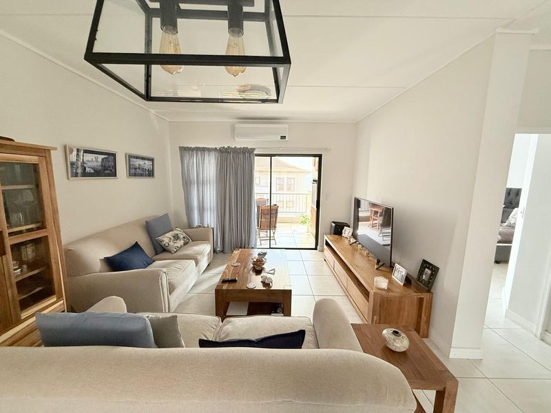 A bright and well-maintained living room featuring tiled flooring, a split-system air conditioner, and a sliding glass door leading to an outdoor balcony.