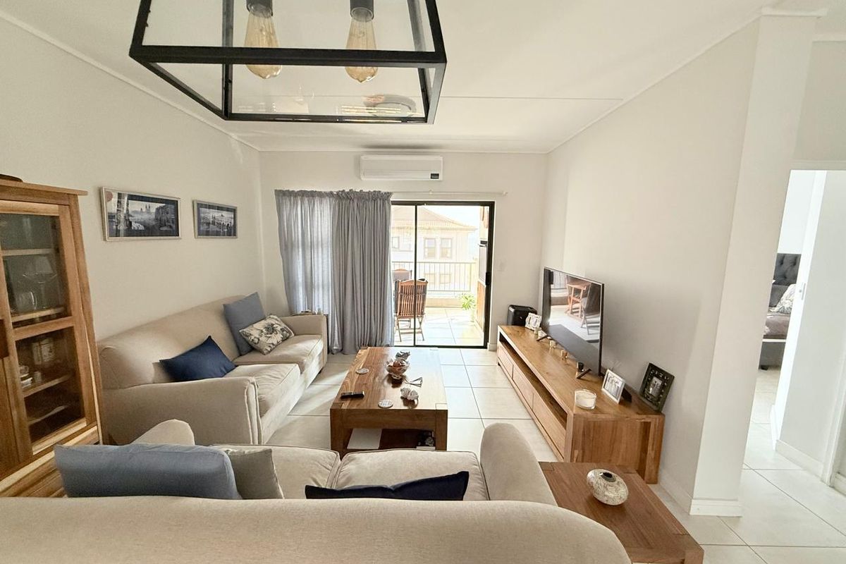 A bright and well-maintained living room featuring tiled flooring, a split-system air conditioner, and a sliding glass door leading to an outdoor balcony.