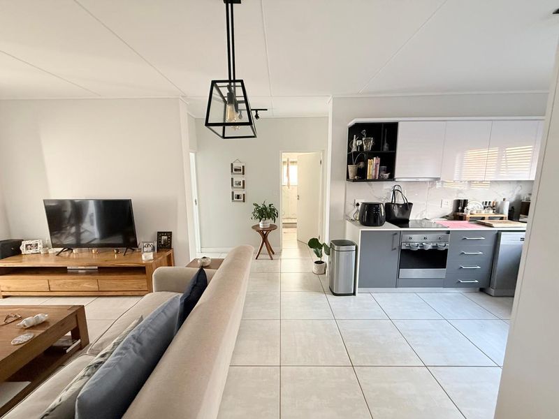 An open-plan living and kitchen area featuring modern grey and white cabinetry, built-in appliances, and neutral tiled flooring throughout.