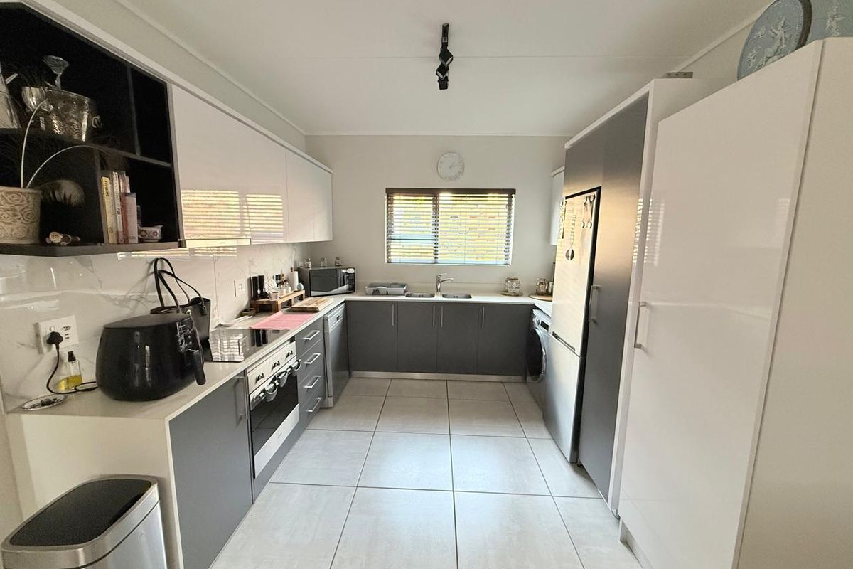 Modern galley-style kitchen featuring sleek white and grey cabinetry, integrated appliances, tiled flooring, and ample counter space with a functional layout.