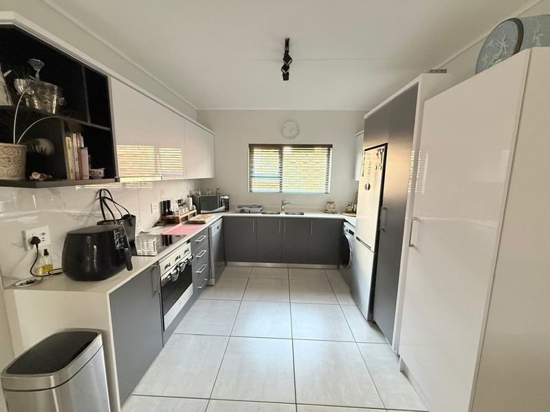 Modern galley-style kitchen featuring sleek white and grey cabinetry, integrated appliances, tiled flooring, and ample counter space with a functional layout.