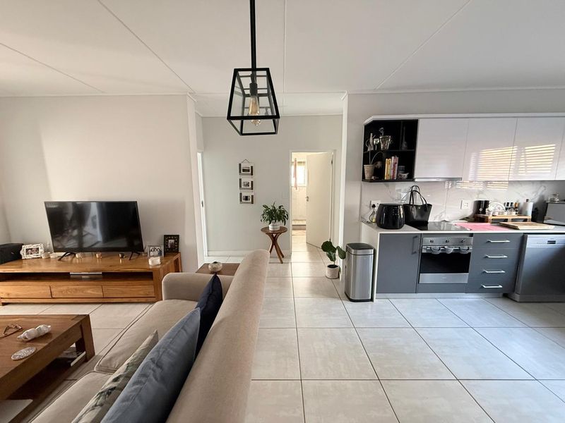 Open-plan living area featuring a modern kitchen with built-in appliances, sleek cabinetry, and neutral tiled flooring throughout the combined space.