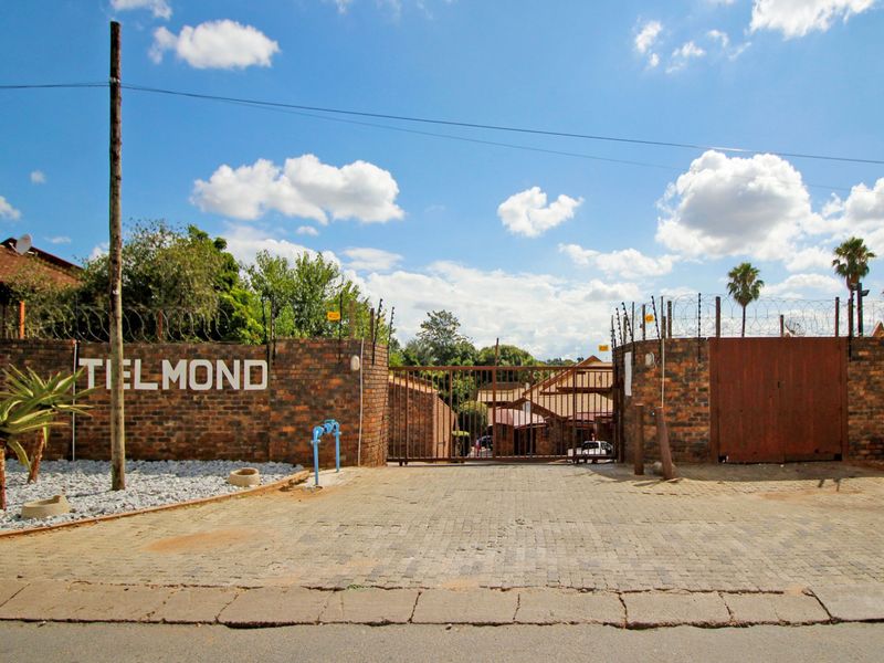 The entrance to Tielmond complex featuring a brick boundary wall, electric fencing, and a metal security gate leading to the townhouse development.