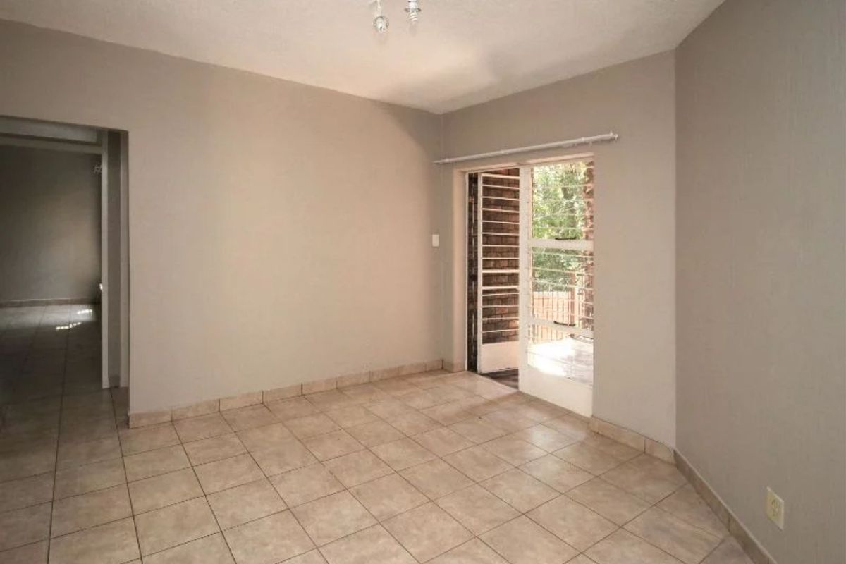 An empty living room featuring neutral tiled flooring and a sliding glass door providing access to an outdoor area.