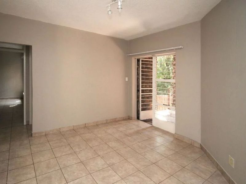 An empty living room featuring neutral tiled flooring and a sliding glass door providing access to an outdoor area.
