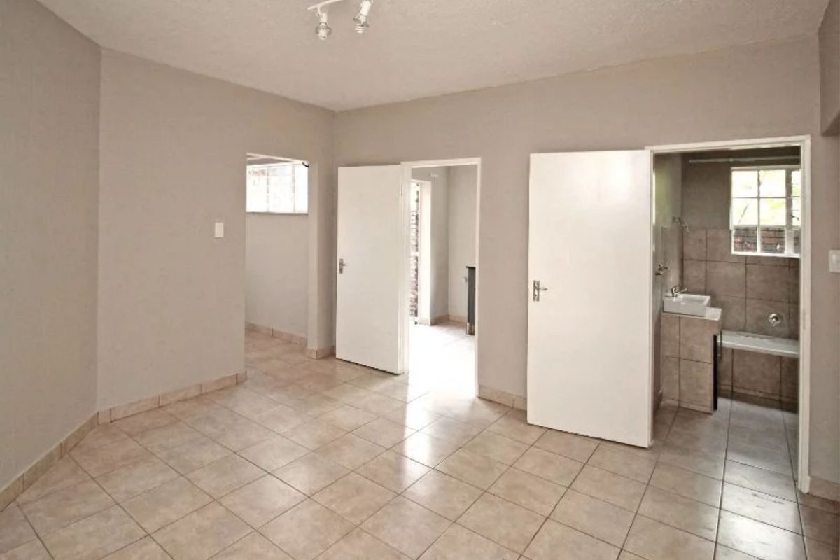 An empty bedroom featuring tiled flooring and an attached en-suite bathroom with a built-in bathtub and vanity.