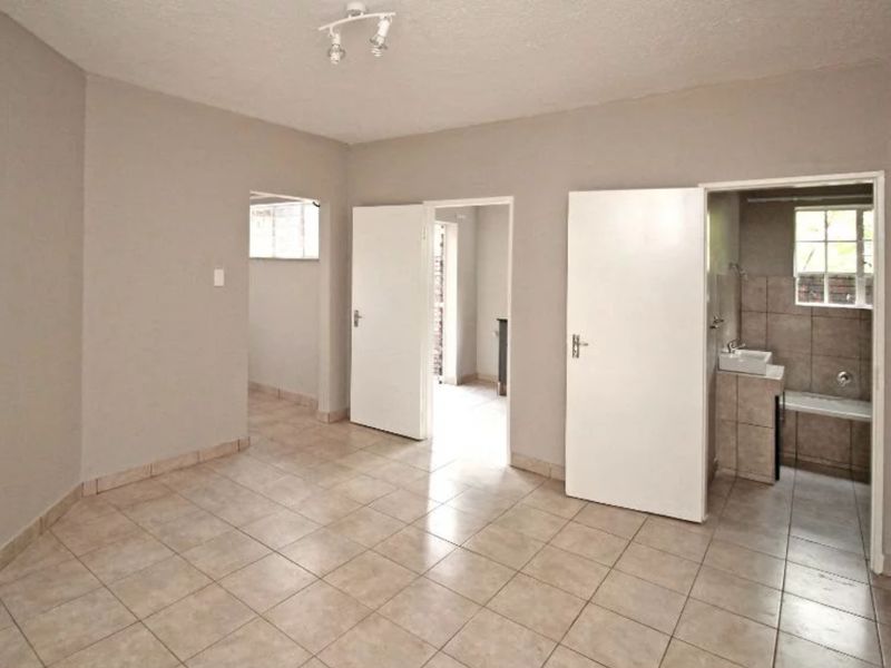 An empty bedroom featuring tiled flooring and an attached en-suite bathroom with a built-in bathtub and vanity.