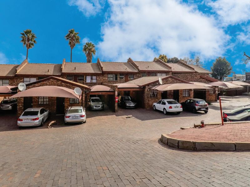 Front exterior view of a townhouse complex featuring brick facades, tiled roofing, and covered parking bays with paved driveway access.