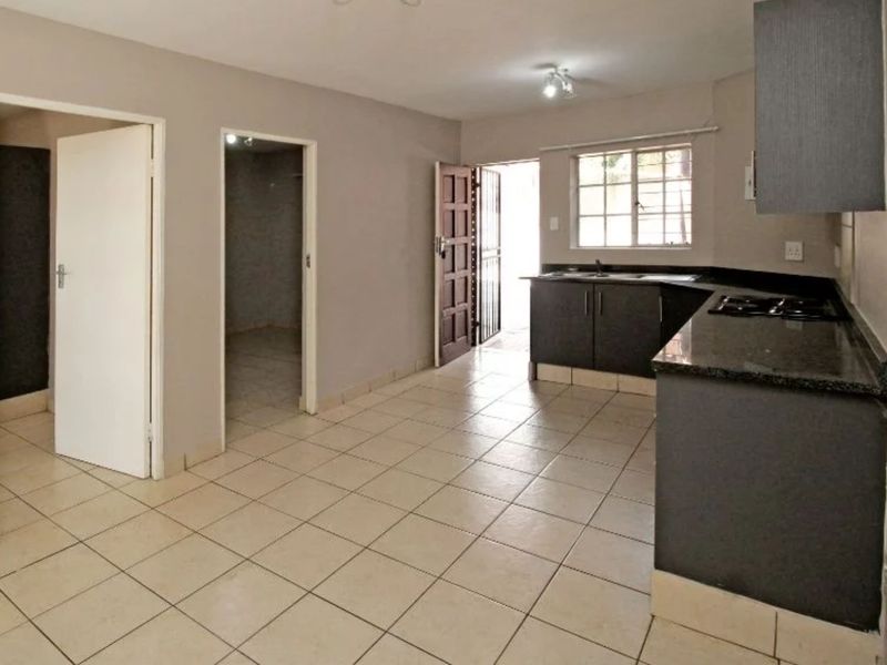 Open-plan kitchen and living area featuring tiled flooring, dark cabinetry with granite countertops, and direct access to an exterior security gate.