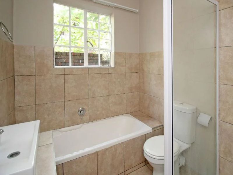 A functional bathroom featuring a built-in bathtub, a separate shower enclosure, and neutral wall tiling.