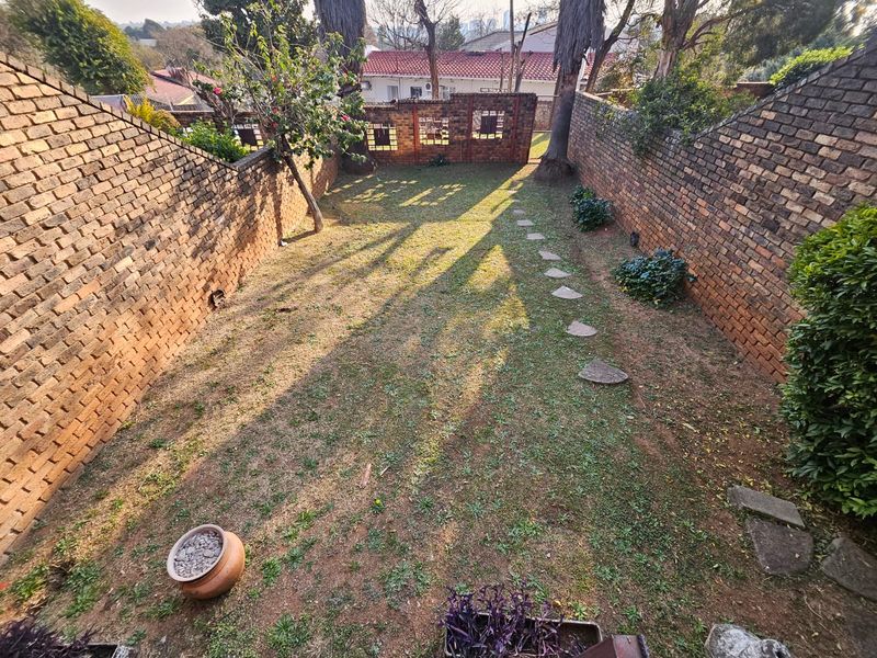 A private rear garden featuring high brick boundary walls, a decorative brick screen, and a stone pathway leading through a lawn area.