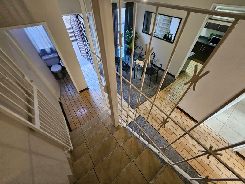An elevated view of an open-plan living area featuring tiled flooring, a staircase with security gate, and access to a kitchen and guest toilet.