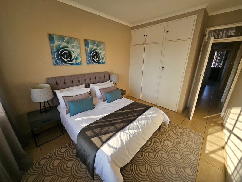 A well-lit bedroom featuring built-in cupboards and neutral tiled flooring, offering a comfortable and functional living space.