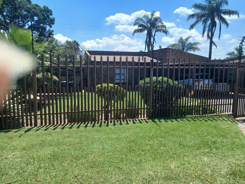 Front view of a brick house featuring a well-maintained lawn and secure steel palisade fencing.