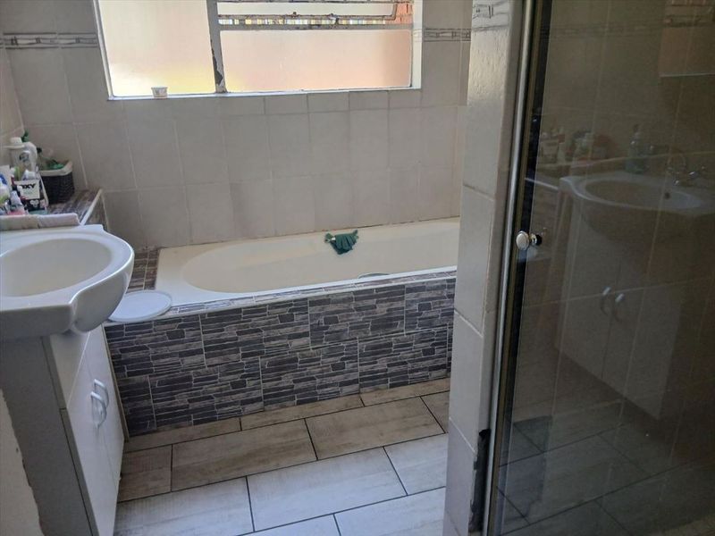 A functional bathroom featuring a built-in bathtub with decorative tiling, a vanity basin, and a separate shower enclosure.