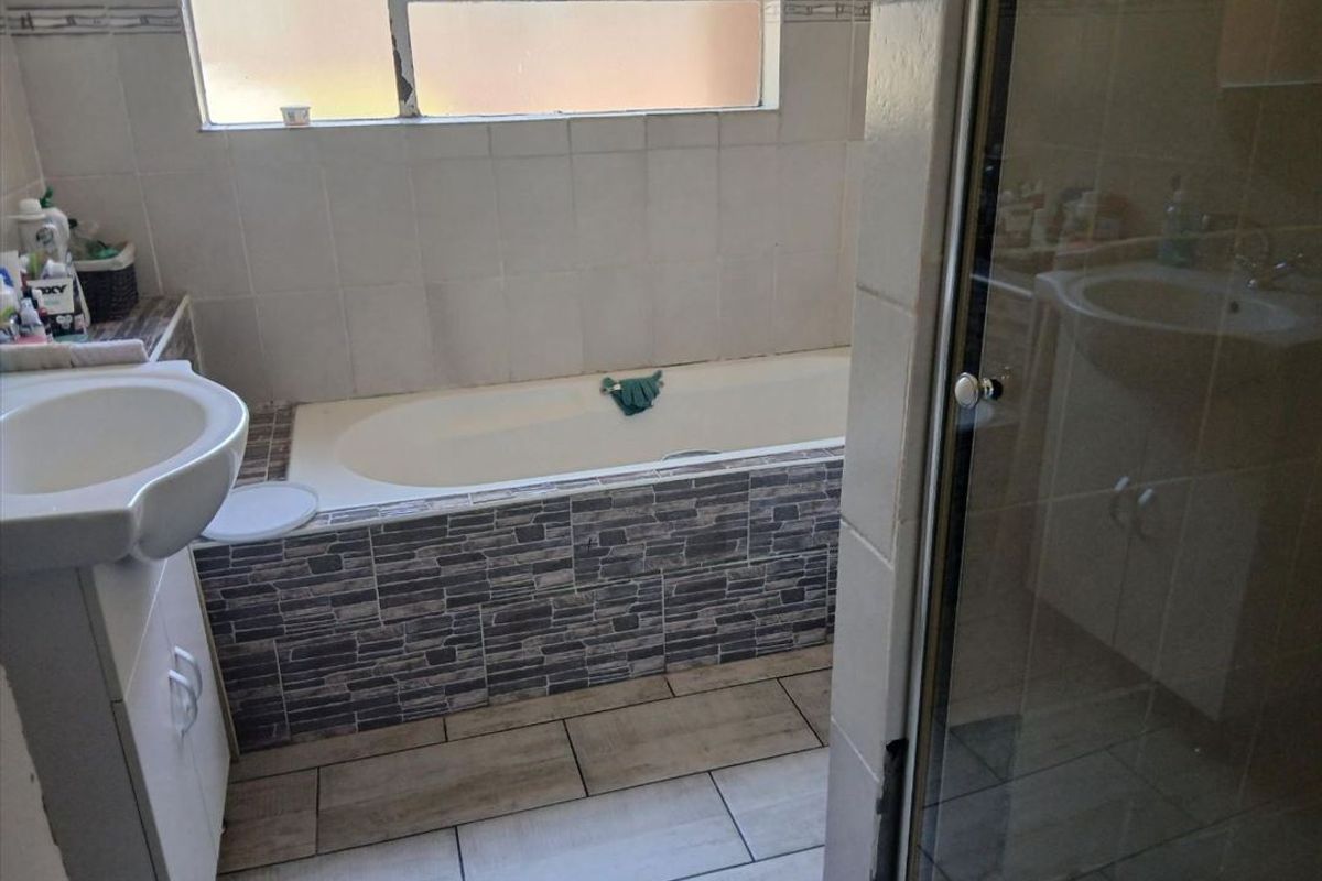 A functional bathroom featuring a built-in bathtub with decorative tiling, a vanity basin, and a separate shower enclosure.