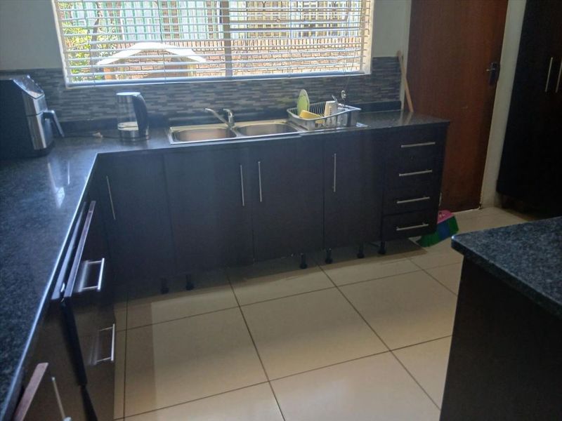 A functional kitchen featuring dark wood cabinetry, granite countertops, a double sink, and a mosaic tile backsplash with tiled flooring.