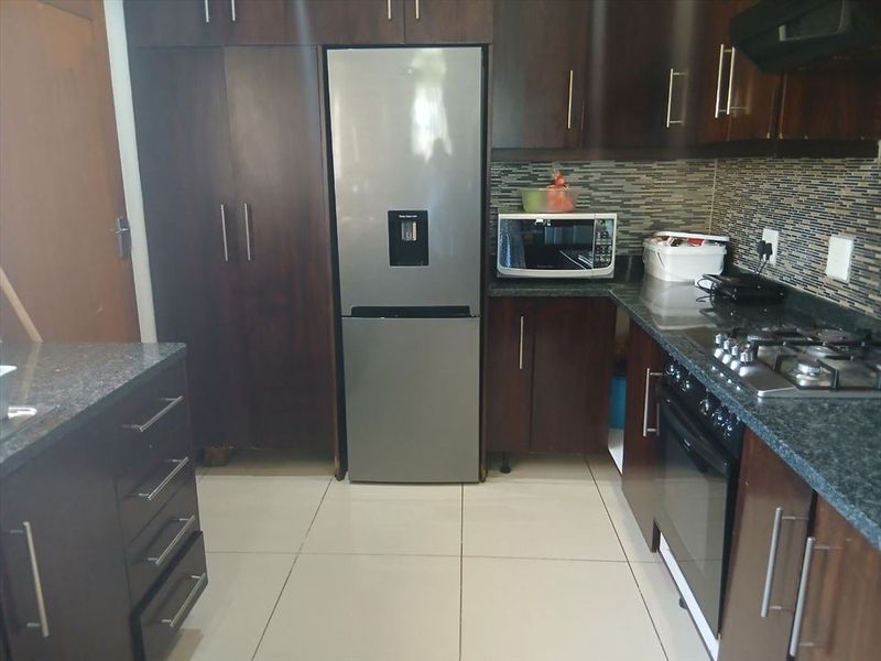 A functional kitchen featuring dark wood cabinetry, granite countertops, a mosaic tile backsplash, and integrated appliances including an oven and gas hob.