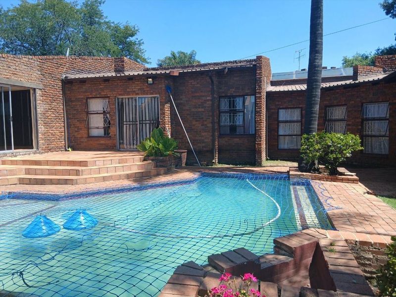 Rear exterior view featuring a swimming pool with safety net, brick facade, and a raised tiled patio area.