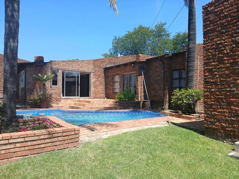 Rear exterior view featuring a swimming pool, brick facade, and tiled patio area with direct access to the home through sliding glass doors.