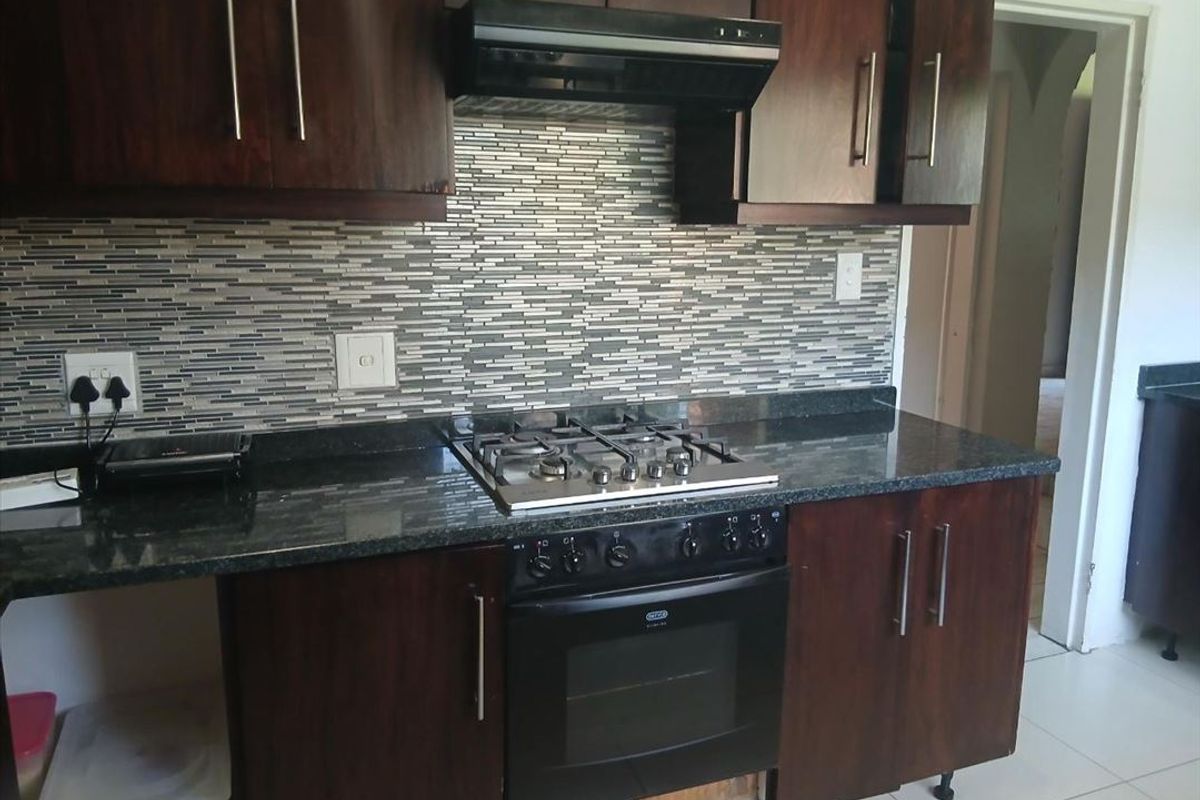 A functional kitchen featuring dark wood cabinetry, granite countertops, a gas hob, built-in oven, and a modern mosaic tile backsplash.