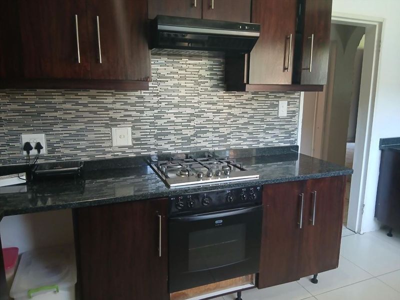 A functional kitchen featuring dark wood cabinetry, granite countertops, a gas hob, built-in oven, and a modern mosaic tile backsplash.