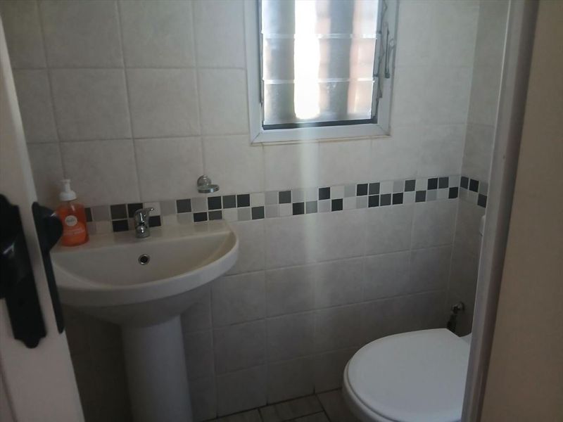 A compact bathroom featuring a pedestal basin, toilet, and neutral tiled walls with a decorative mosaic border.
