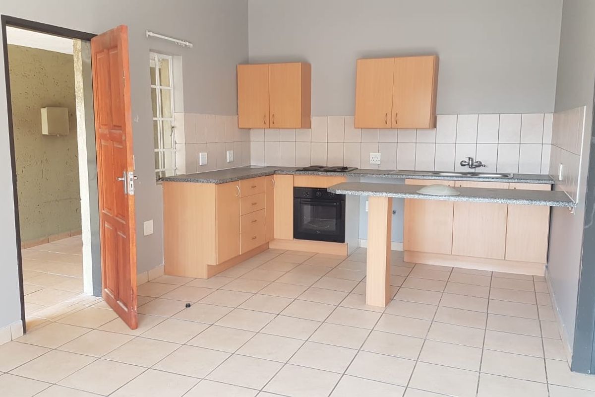 A functional kitchen featuring light wood cabinetry, laminate countertops, built-in oven, electric hob, and a double sink with tiled backsplash.