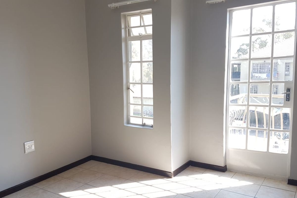 An empty living area featuring neutral walls, tiled flooring, and a glass-paned french door providing access to an outdoor space.