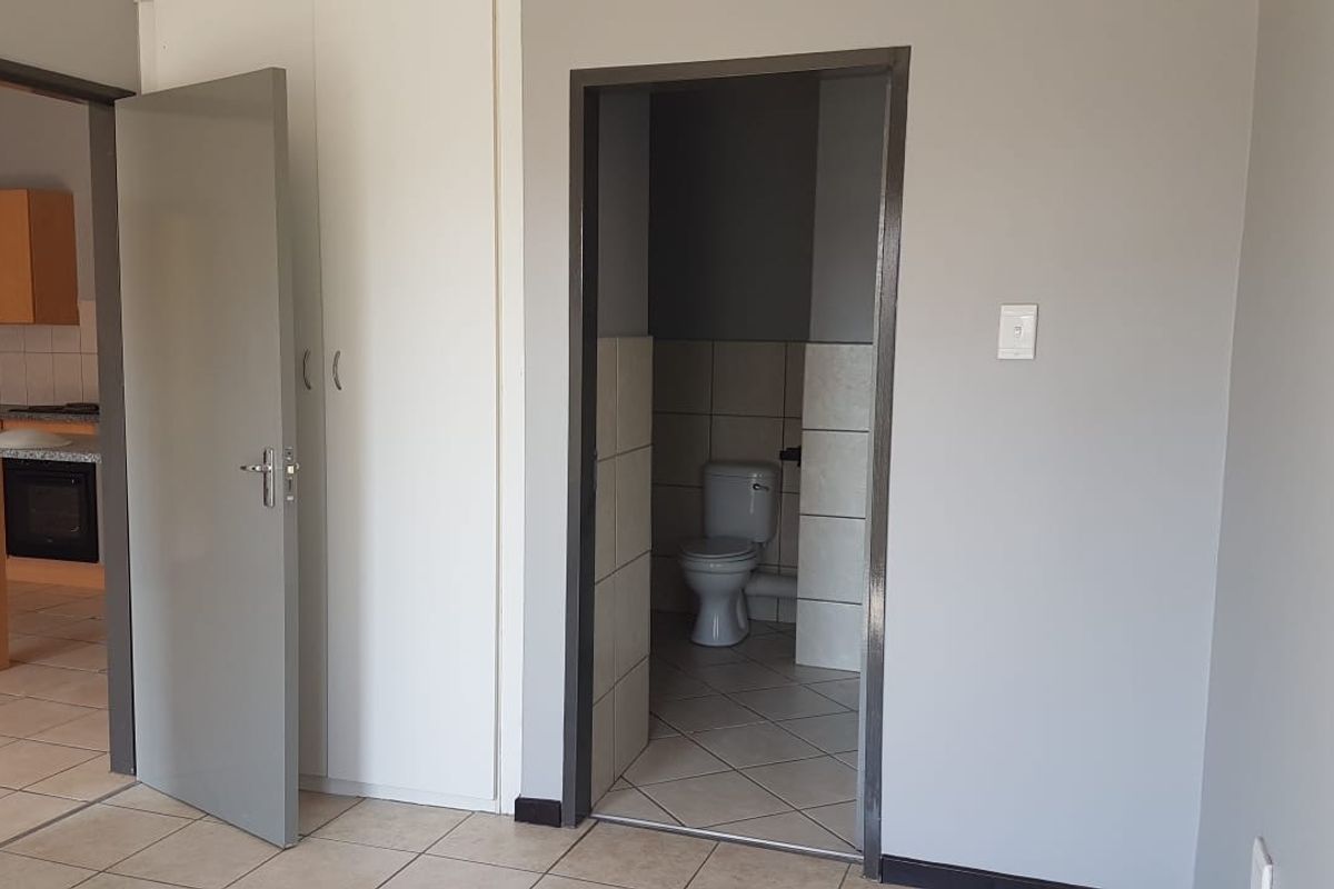 Open plan living area featuring tiled floors, built-in storage, and a view into the kitchen and adjacent bathroom with a toilet.