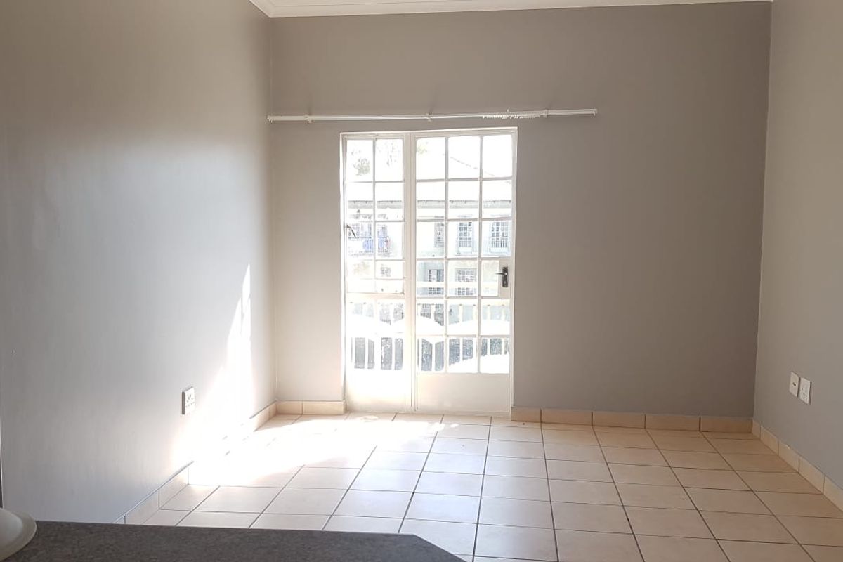 An empty living room featuring neutral wall paint, tiled flooring, and glass-paned french doors providing natural light and access to the exterior.