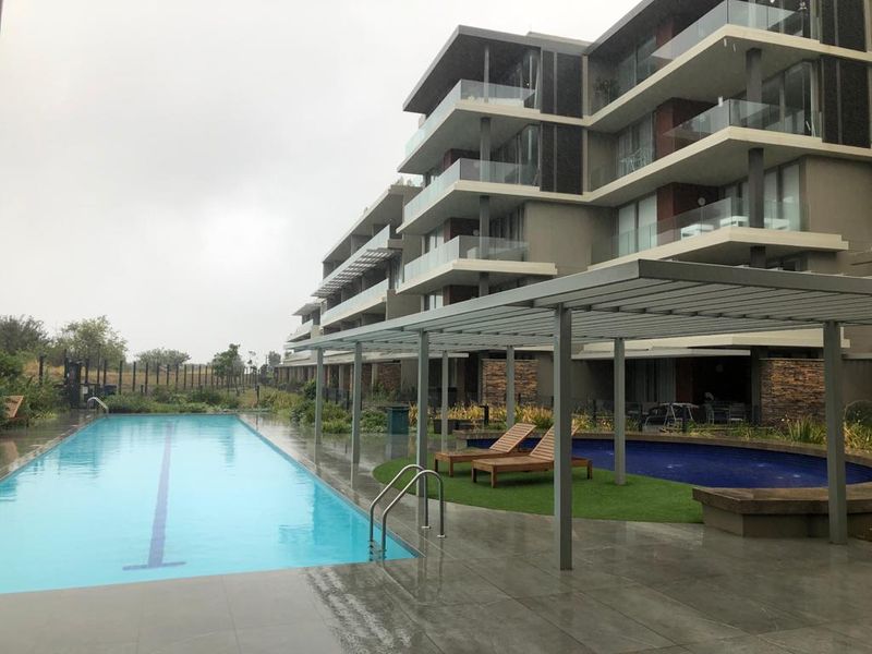 Modern apartment complex featuring a lap pool, circular splash pool, and a covered pergola area with contemporary architectural finishes.