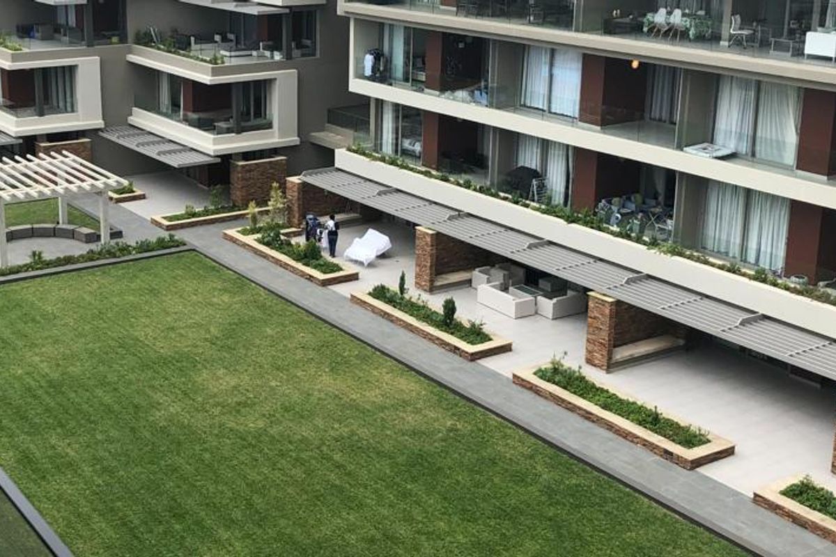 Elevated view of a modern apartment complex featuring a well-maintained central lawn, stone-clad patio areas, and private balconies with glass railings.