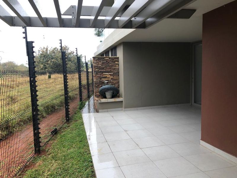 A covered patio area featuring tiled flooring, a stone accent wall, and a pergola, overlooking a fenced outdoor space.