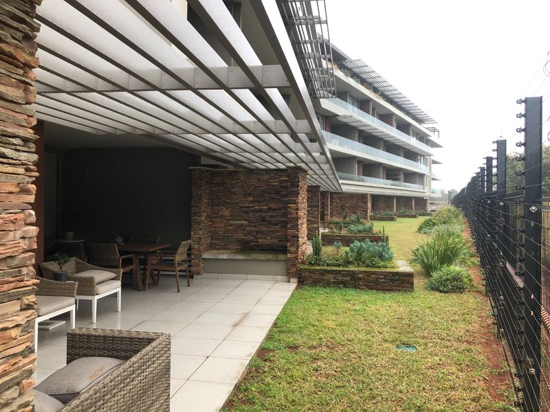 Spacious covered patio featuring stone-clad pillars, a pergola roof, and direct access to a landscaped garden area with secure perimeter fencing.